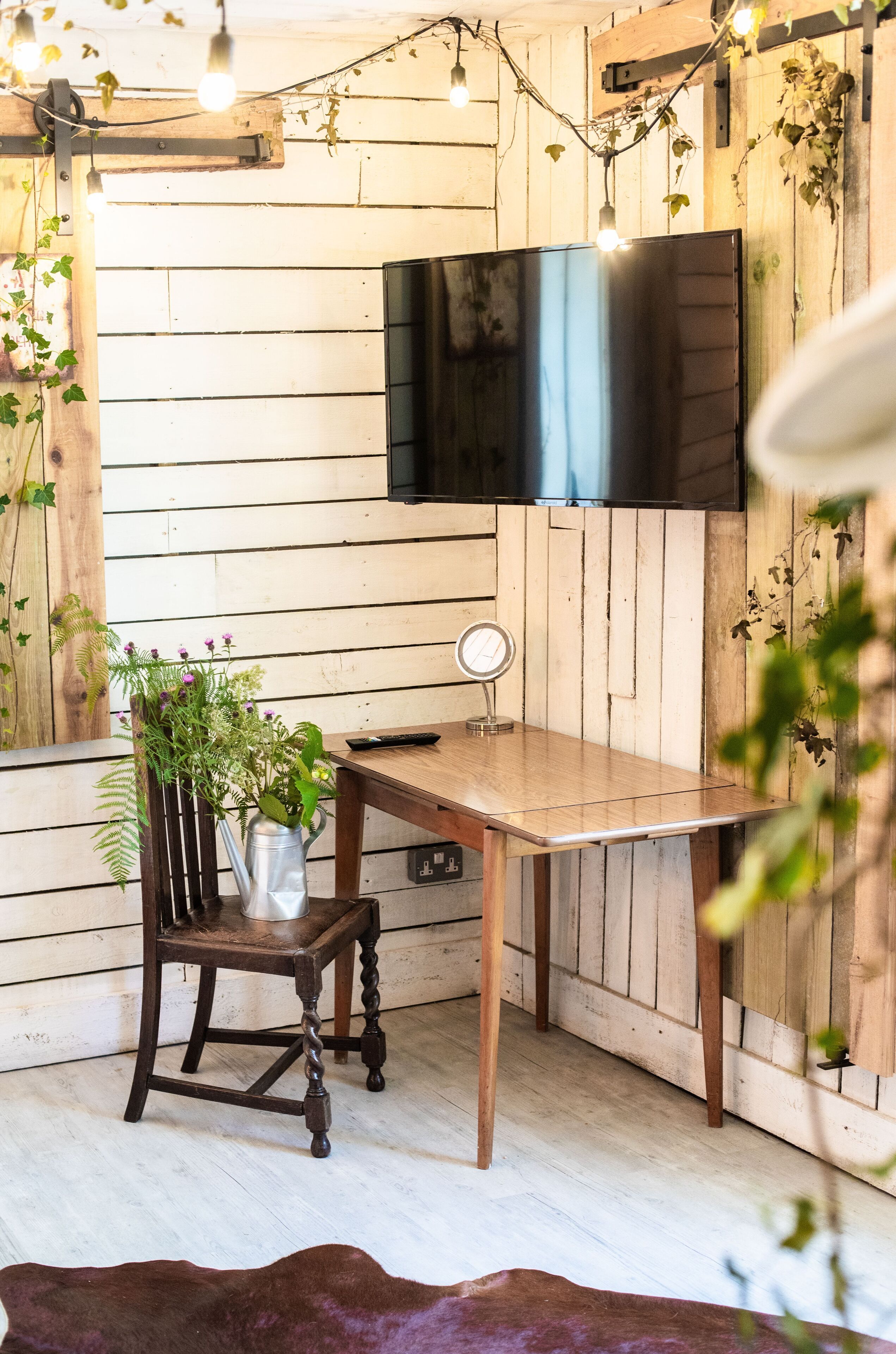 A rustic wooden room with a table, chair, and a TV mounted on the wall.