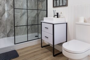 A modern bathroom with a white sink, black cabinet, and a glass shower enclosure. - James Place @ Pontmorlais (Merthyr Tydfil)