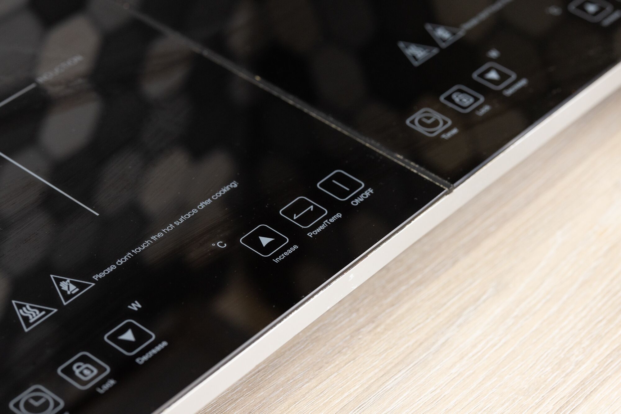 A close-up of a black control panel with various icons and text, including a warning about hot surfaces and options to increase or decrease temperature.