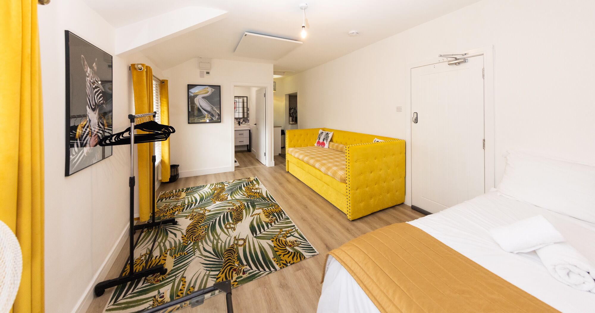 A hotel room with a bed, a sofa, a small desk, and a bathroom.