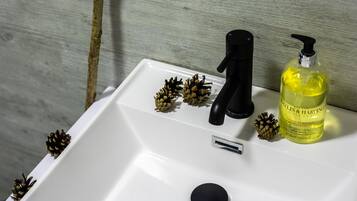 A white bathroom sink with a black faucet, a bottle of hand soap, and pine cones on the edge.