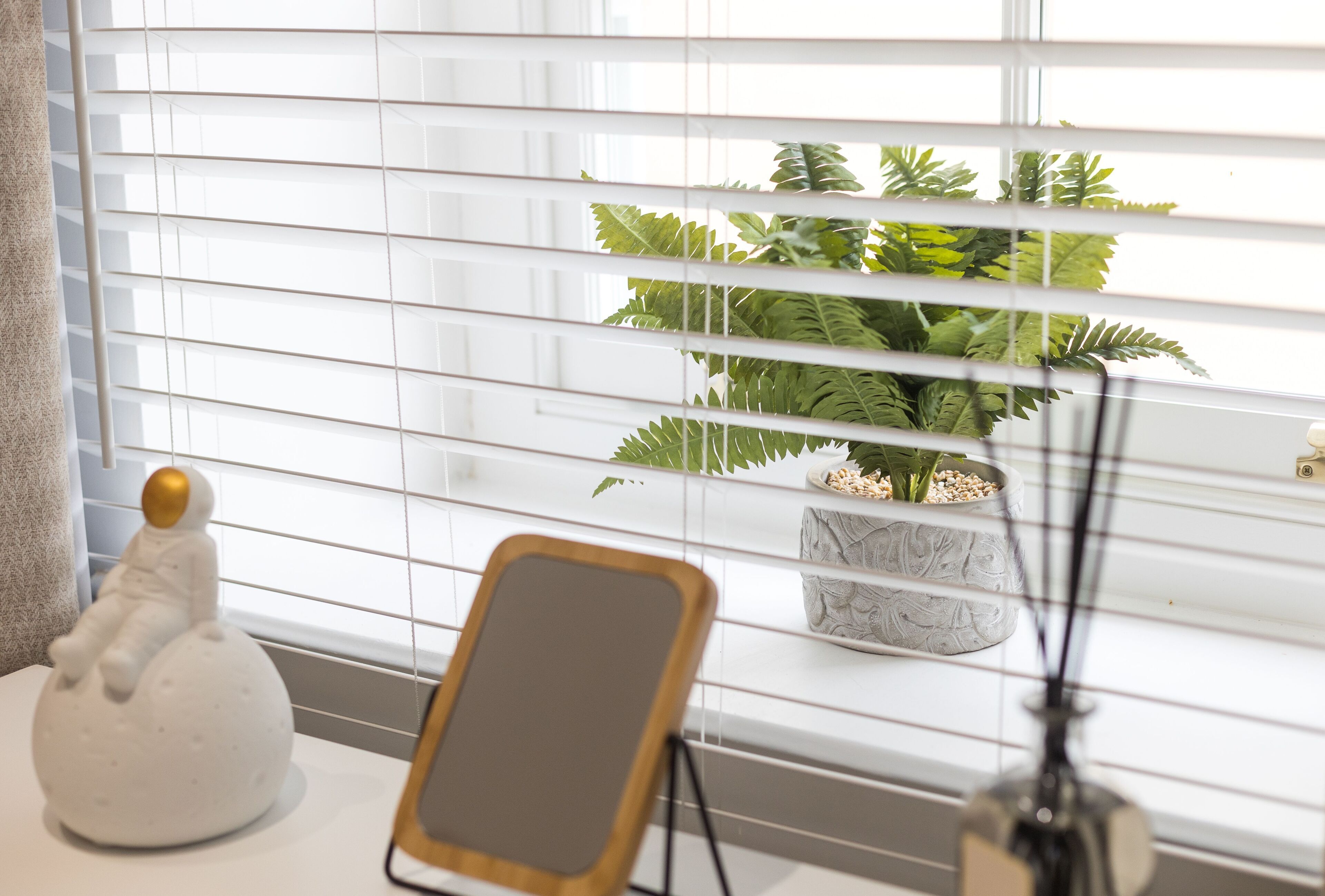 Et vindue med skodder, en potteplante og en lille figur på et bord.