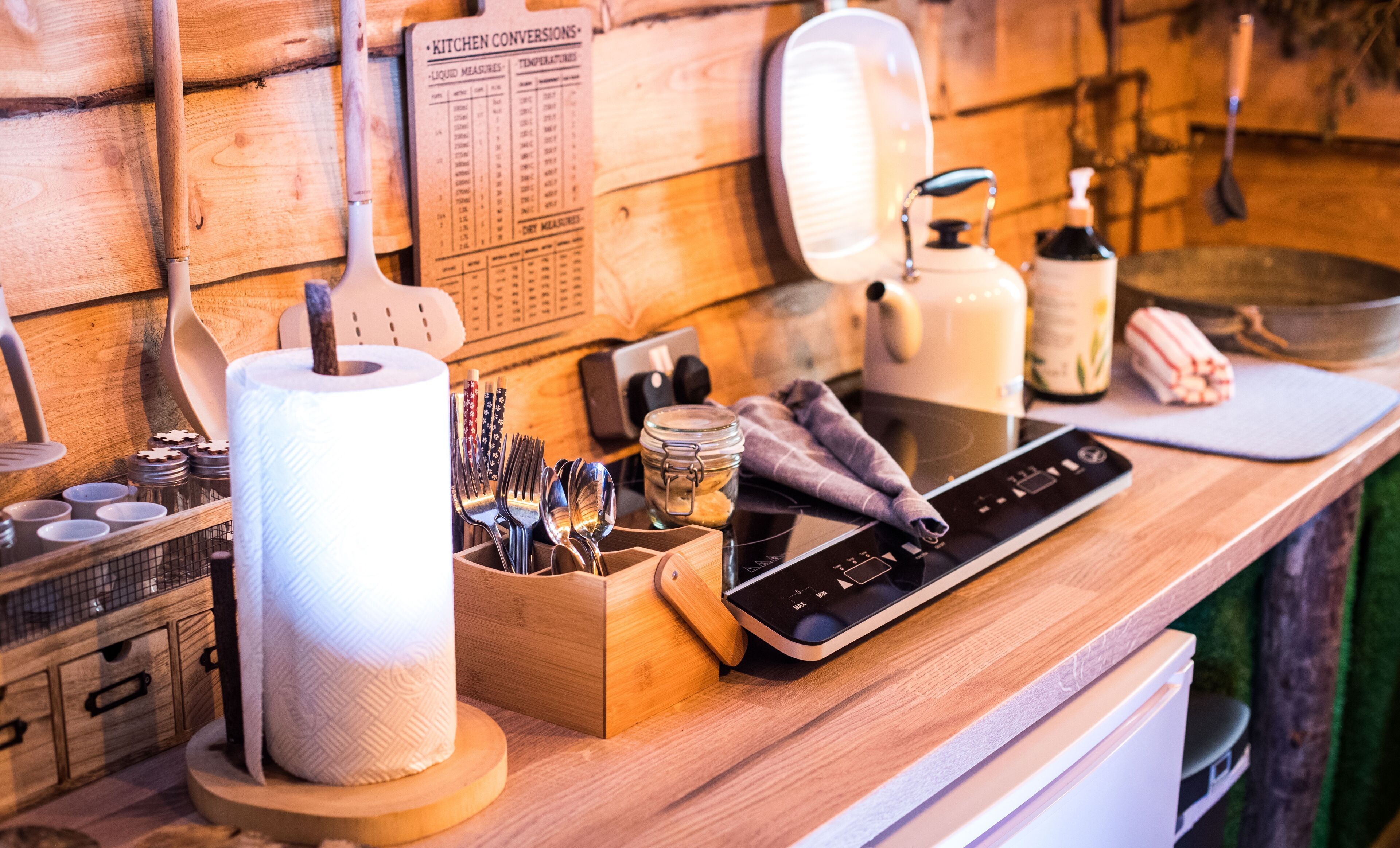 Una encimera de cocina con una balanza digital, un dispensador de toallas de papel, un estante para especias y una tabla de cortar de madera.