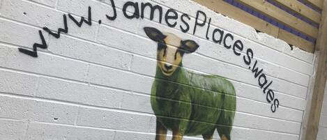 A wall with a mural of a sheep and the text "www.JamesPlacesWales".