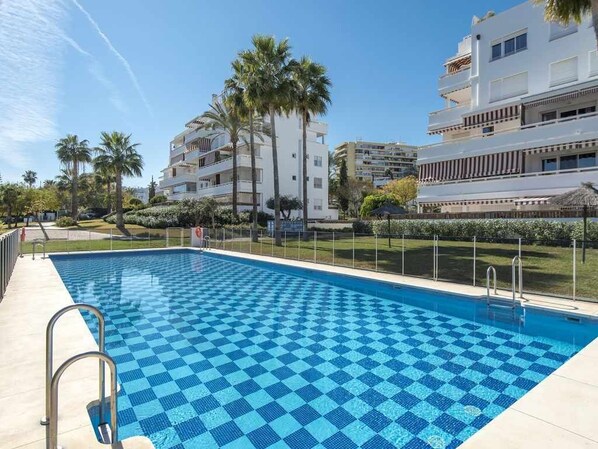 A swimming pool with a checkered pattern, surrounded by palm trees and modern buildings. - Penthouse with panoramic views Los Alamos (Torremolinos)