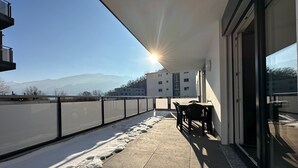 Un balcone con tavolo e sedie, vista sulle montagne e cielo sereno.