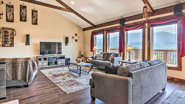 A spacious living room with a large sofa, a television, and a fireplace. There are large windows with curtains, and a wooden ceiling. - Panoramic Mtn Views! Luxe Retreat in Gatlinburg (Gatlinburg)