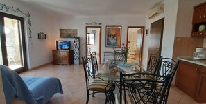 A dining area with a glass table, metal chairs, and a blue tablecloth. There is a television on a wooden cabinet, and artwork on the walls. - Villa Linet (Funtana)