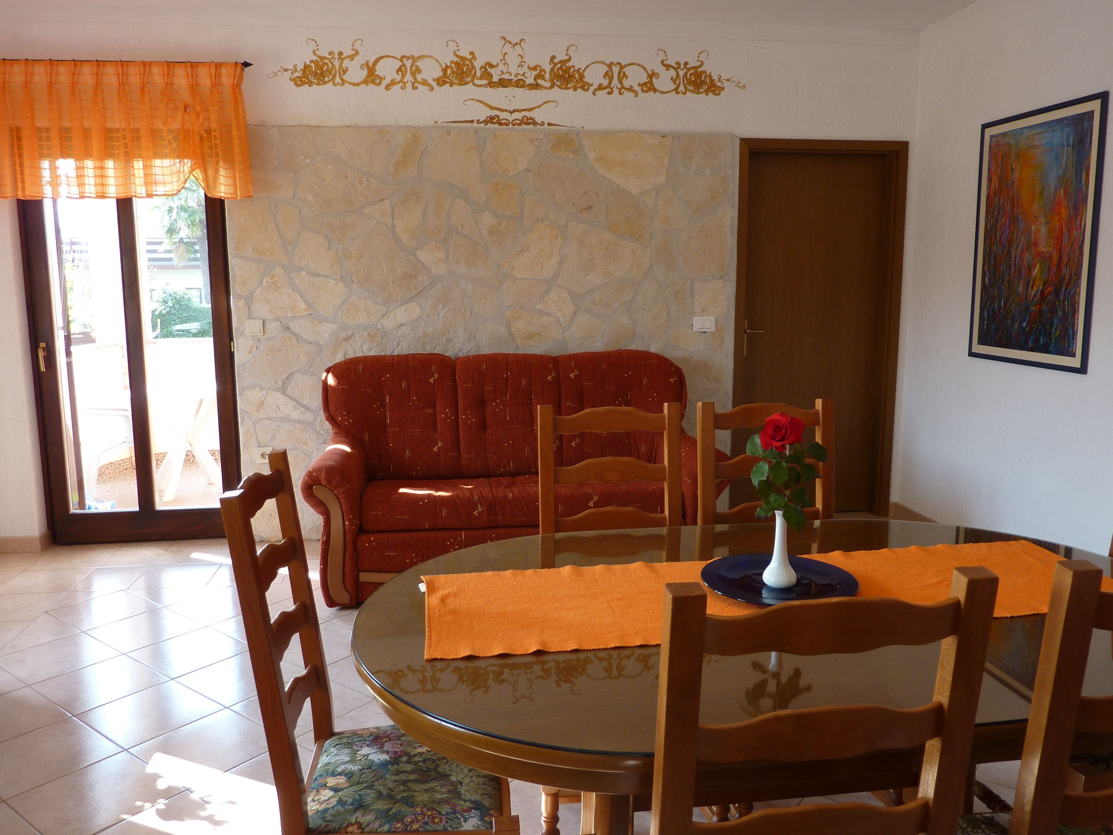 A dining area with a round glass table, wooden chairs, a red sofa, and a stone wall.