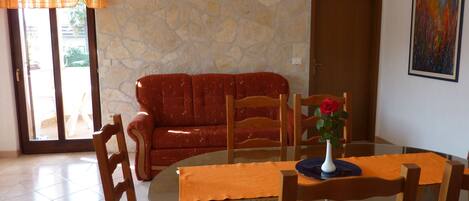 A dining area with a round glass table, wooden chairs, a red sofa, and a stone wall.
