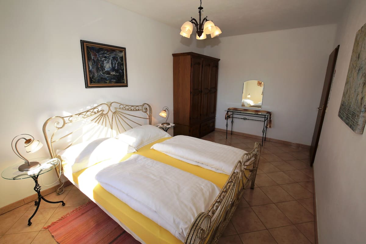 A bed with white and yellow bedding, a wooden cabinet, a bedside table with a lamp, and a painting on the wall.