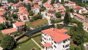 Vista aérea de una zona residencial costera con casas, un edificio central con techo rojo y una masa de agua al fondo.