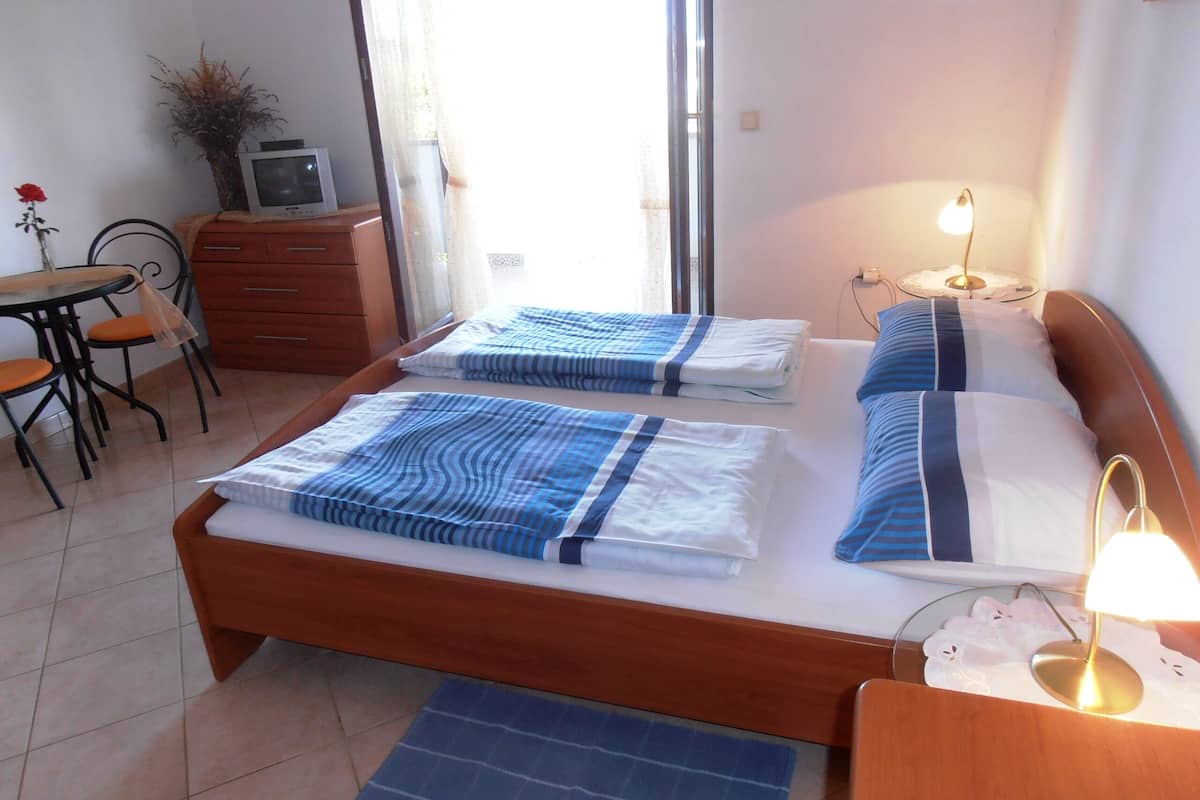 A bedroom with two beds, a small table with a chair, a TV, and a lamp.