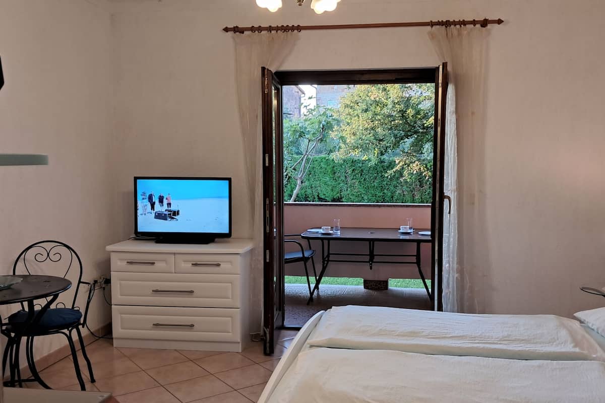 A hotel room with a bed, a TV, a desk, and a view of the outdoors.