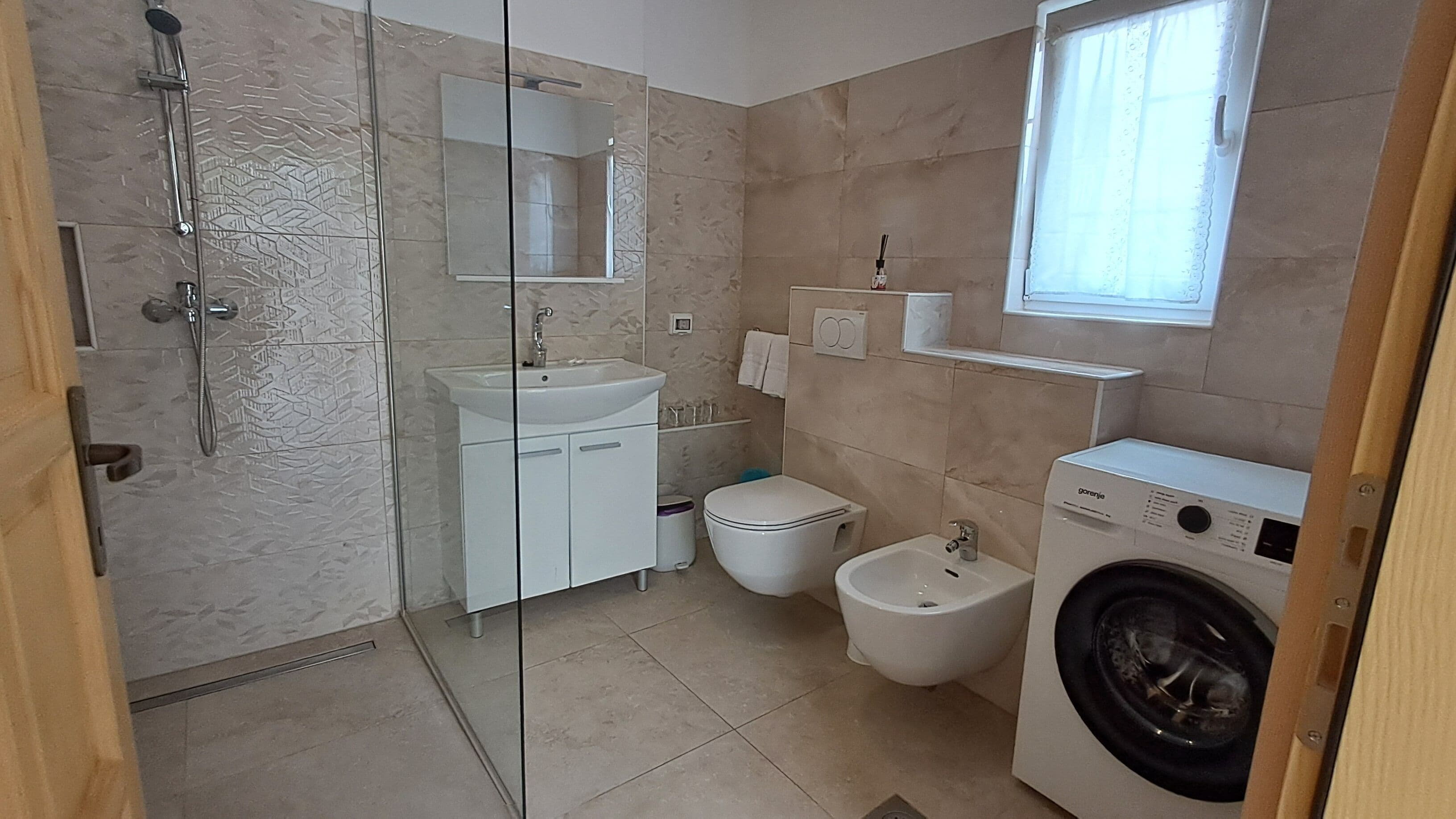 Un baño con cabina de ducha de vidrio, un lavabo, un inodoro, un bidé y una lavadora.