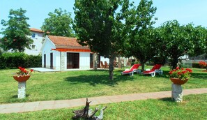 A house with a tiled roof, stone pillars, and a lawn with red lounge chairs. - Holiday home Linet (Funtana)