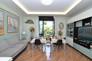 A dining area with a table set for four, a sofa, a TV, and artwork on the walls. - SUPERIOR CASERTA SUITE (Caserta)