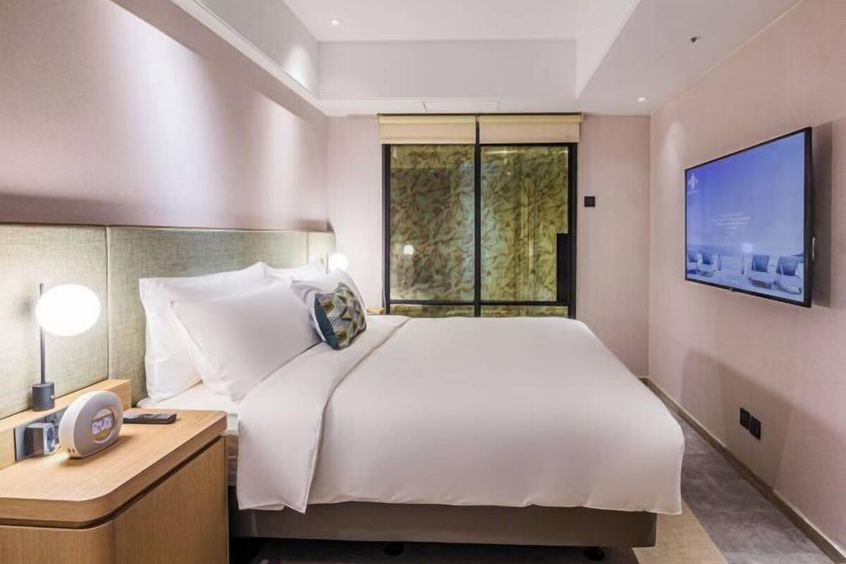 Een moderne hotelkamer met een bed, nachtkastje met een lamp, een aan de muur bevestigde televisie en een raam met uitzicht.
