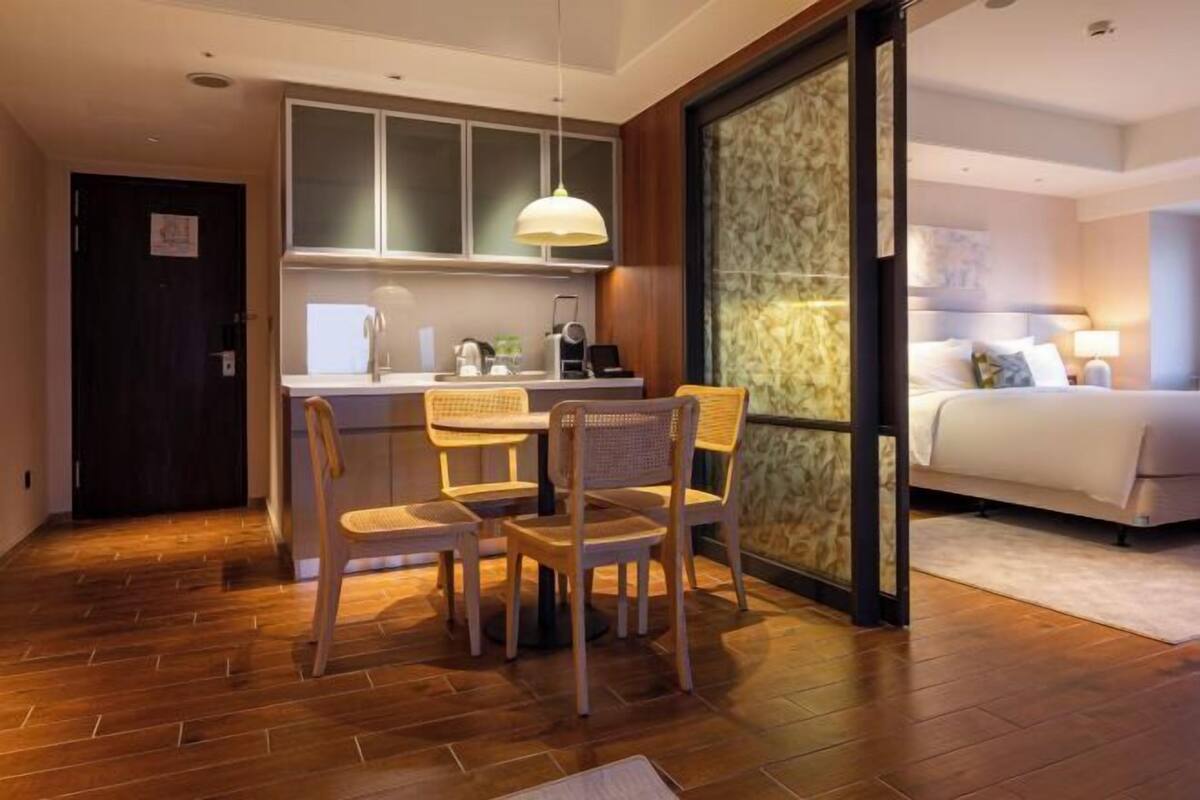 Een compacte hotelkamer met een eethoek, inclusief een tafel en stoelen, een kitchenette en een bed met nachtkastje.
