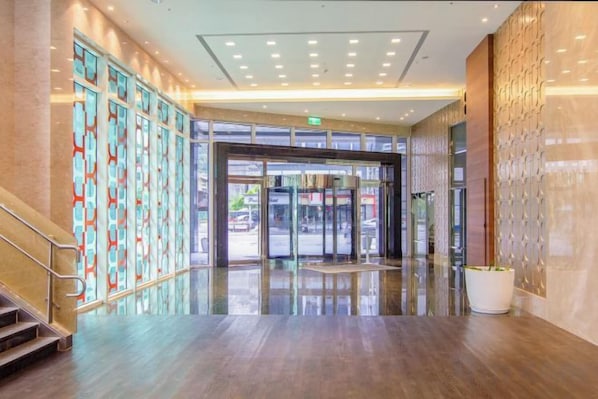 A spacious lobby with a glass door entrance, a staircase, and a potted plant.