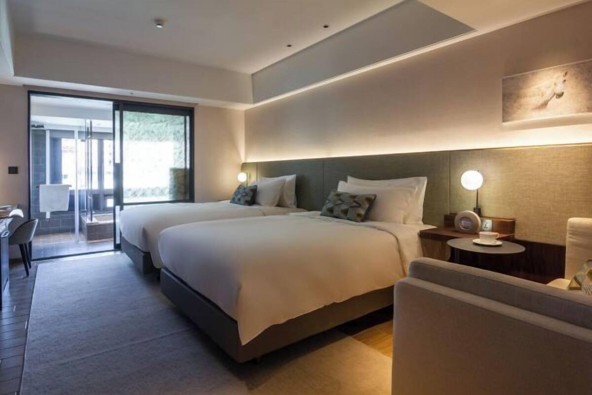 Een moderne hotelkamer met twee bedden, een bureau, een stoel en een kleine tafel met een lamp.