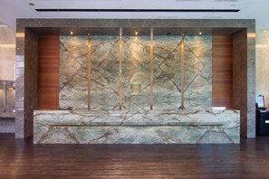 A reception area with a marble wall, wooden paneling, and a seating bench. - Kilin Hotel JiaoXi (Jiaoxi)