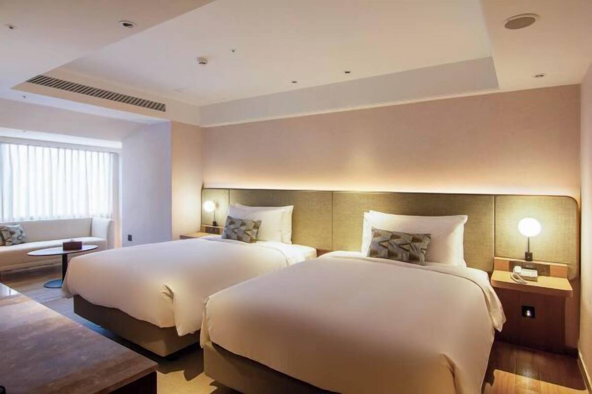 Een hotelkamer met twee bedden, een slaapbank, een klein tafeltje en een nachtkastje met een lamp.