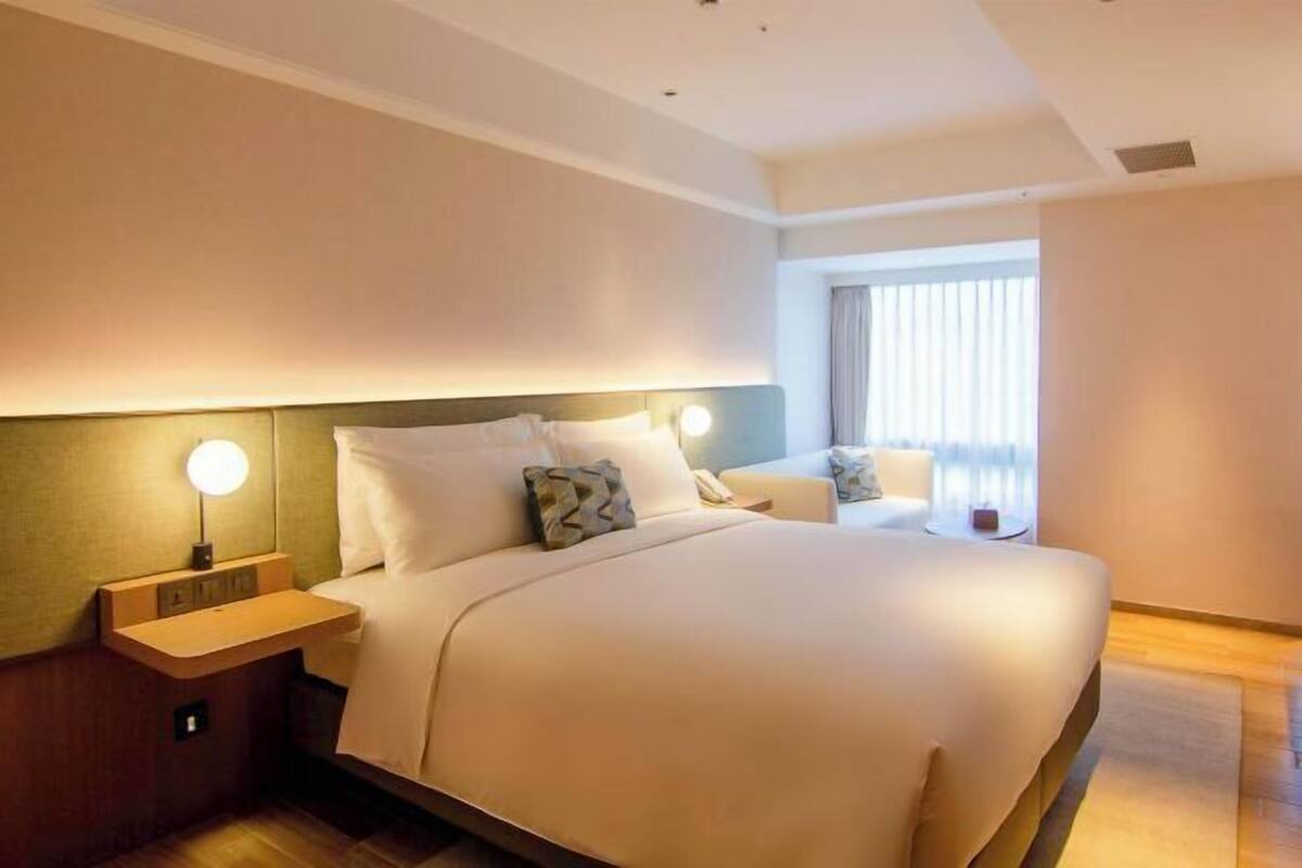 Een hotelkamer met een groot bed, nachtkastjes met lampen, een raam met gordijnen en uitzicht.