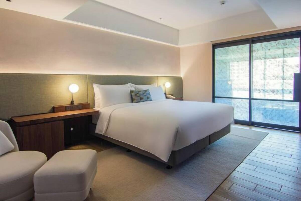 Een moderne hotelkamer met een groot bed, nachtkastjes, een zithoek en een groot raam.