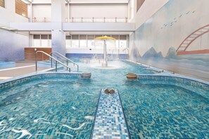 An indoor swimming pool with a diving board, a water slide, and a mural on the wall.