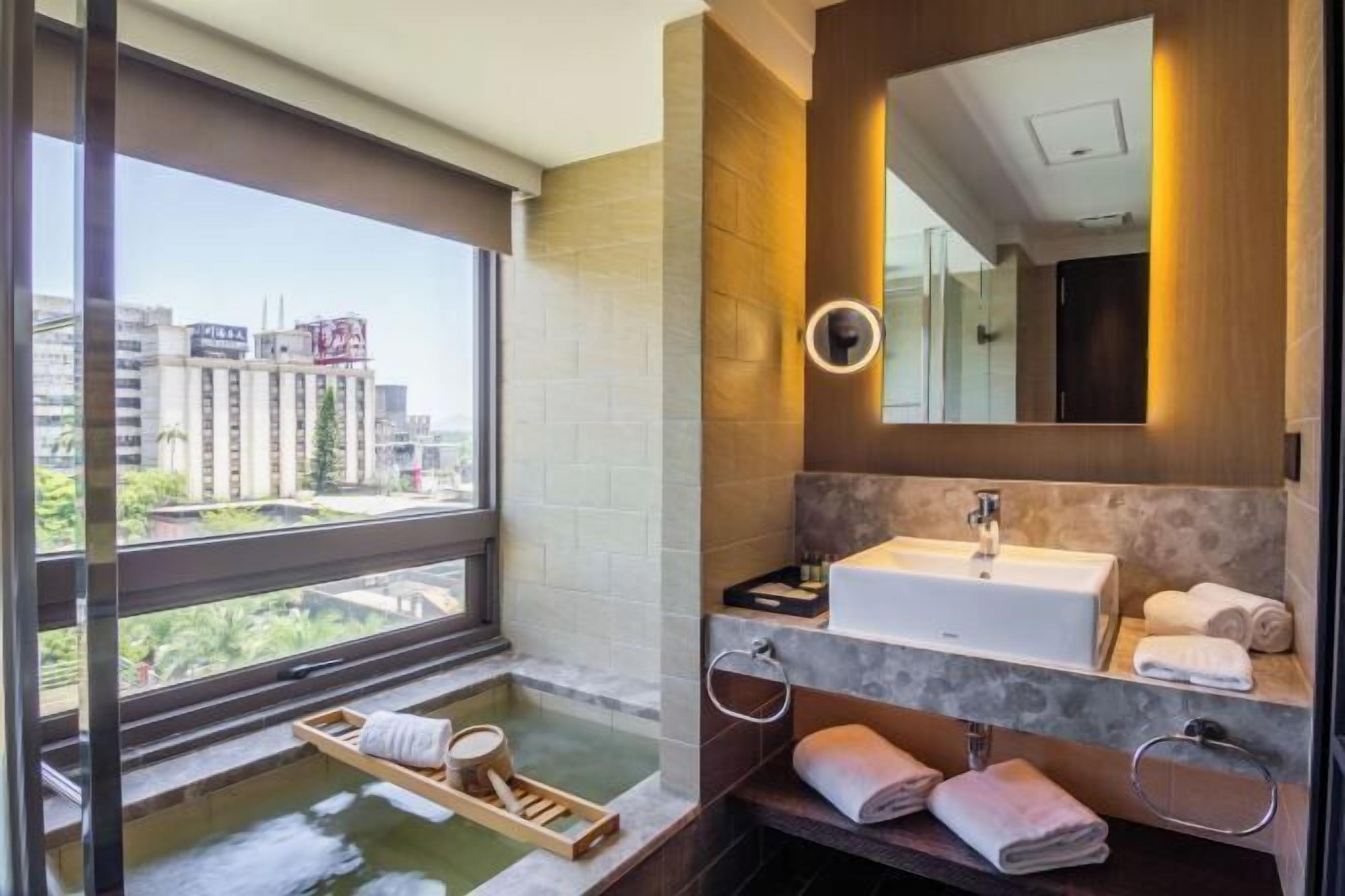 A modern bathroom with a large window, a bathtub, a sink, and a mirror.