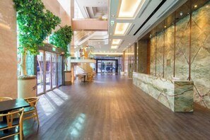 A spacious lobby with a wooden floor, a seating area with tables and chairs, a marble reception desk, and a large glass door leading outside. - Kilin Hotel JiaoXi (Jiaoxi)