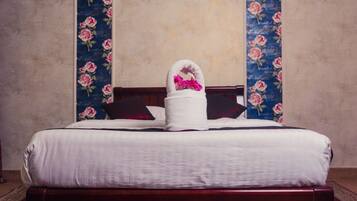 A neatly made bed with a white duvet and a white towel with pink flowers, flanked by two vertical floral wall panels.