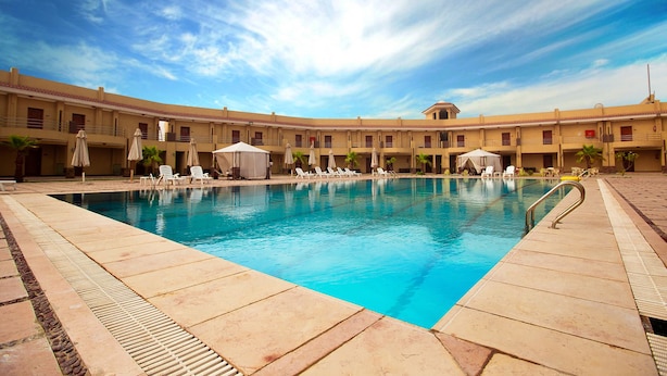 Un espace piscine doté de chaises longues et de parasols, entouré d’un bâtiment comportant de nombreux balcons.