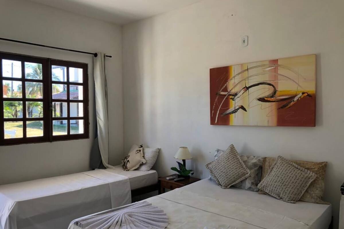Ein Hotelzimmer mit zwei Betten, einem fensterbelaubten Fenster, einem Bild an der Wand und einem kleinen Tisch mit Lampe.