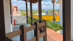 A covered outdoor area with wooden railings, a fire extinguisher, and a view of a yellow building and palm trees.