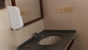 A bathroom with a sink, mirror, towel dispenser, and a towel rack with folded towels.