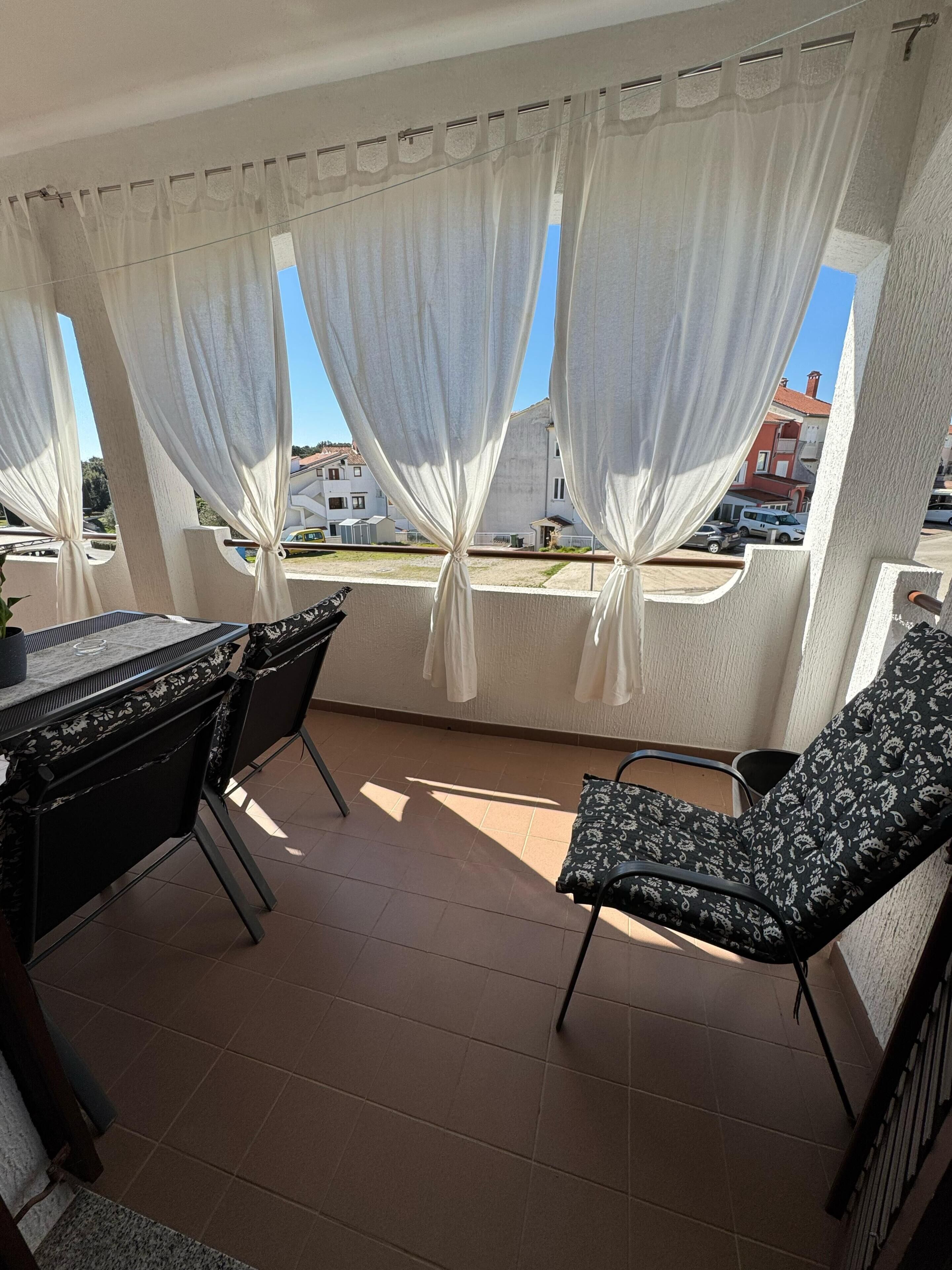 A balcony with a table and chairs, white curtains, and a view of buildings.