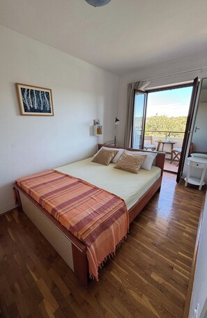 Une chambre à coucher avec un lit, une table de chevet, une lampe, une fenêtre et un balcon.