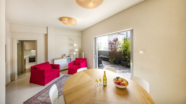 A modern living room with a dining area, red sofas, a wooden dining table, and a view of the outdoors. - Elegant and Airy Apartment One Stop from City Center by VillaRentalsgr (Athens)