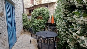 A stone-paved courtyard with a table and chairs, a blue door, and a wall covered in white flowers. - House Nirvana (Vrsar)