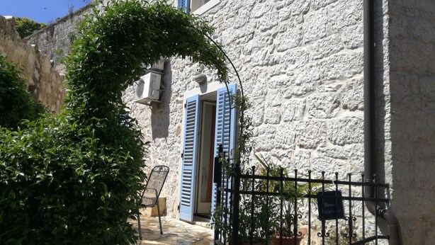 A stone building with blue shutters, a metal gate, and potted plants. - House Nirvana (Vrsar)