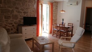 A living room with a stone wall, a television on a cabinet, a dining table with chairs, and a white armchair. - House Nirvana (Vrsar)