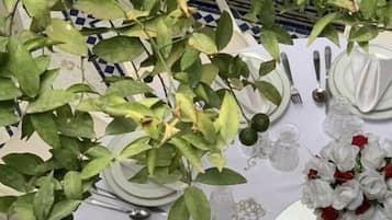 Ein Tisch für eine festliche Veranstaltung, gedeckt mit weißen Tellern, Besteck und einer Mittelstück-Dekoration aus weißen Blumen und einem goldenen Schmuckstück.