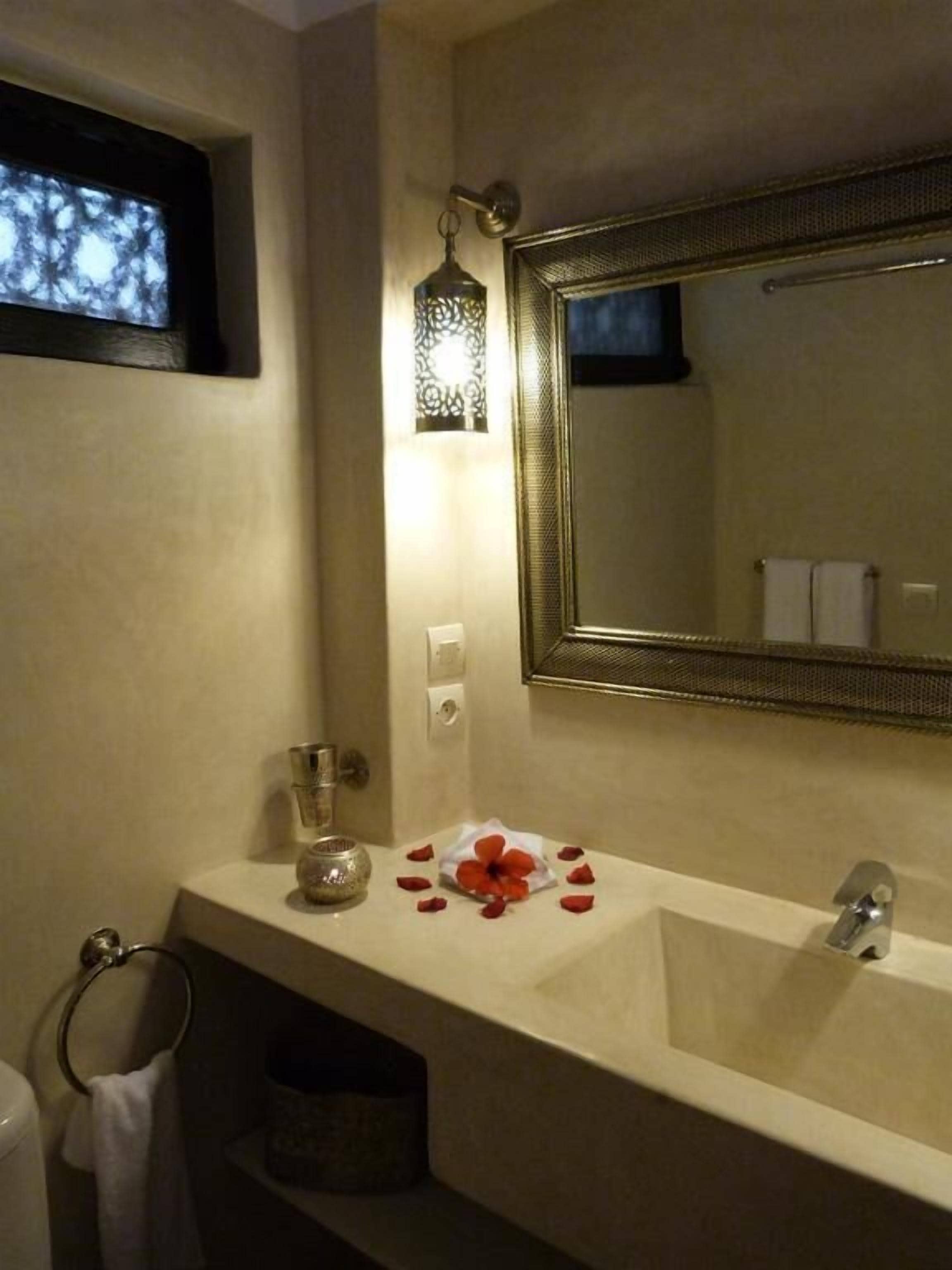 Une salle de bain avec un grand miroir, un lavabo, un porte-serviettes et une lanterne décorative.