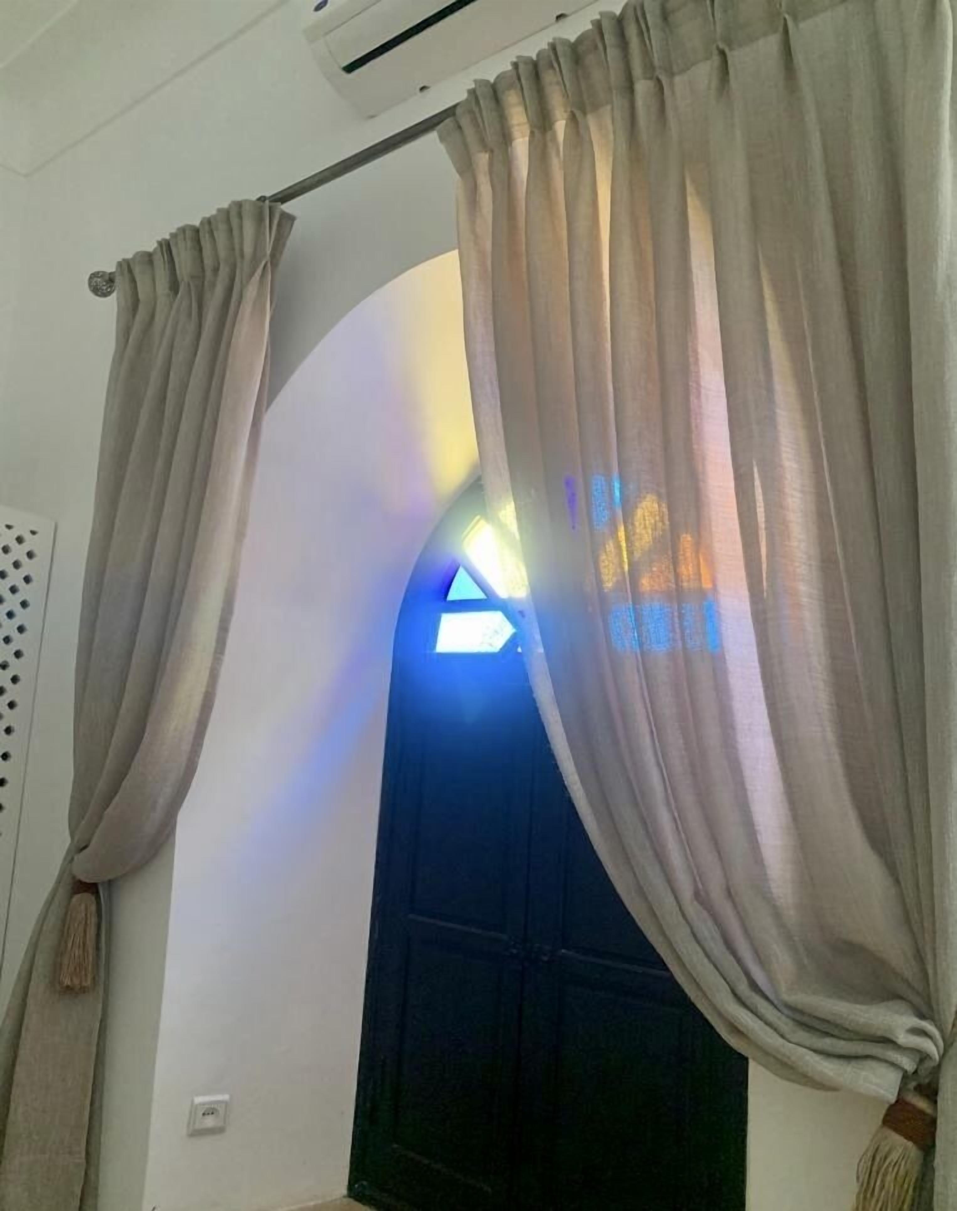 A room with beige curtains, a black door, and a ceiling-mounted air conditioning unit.
