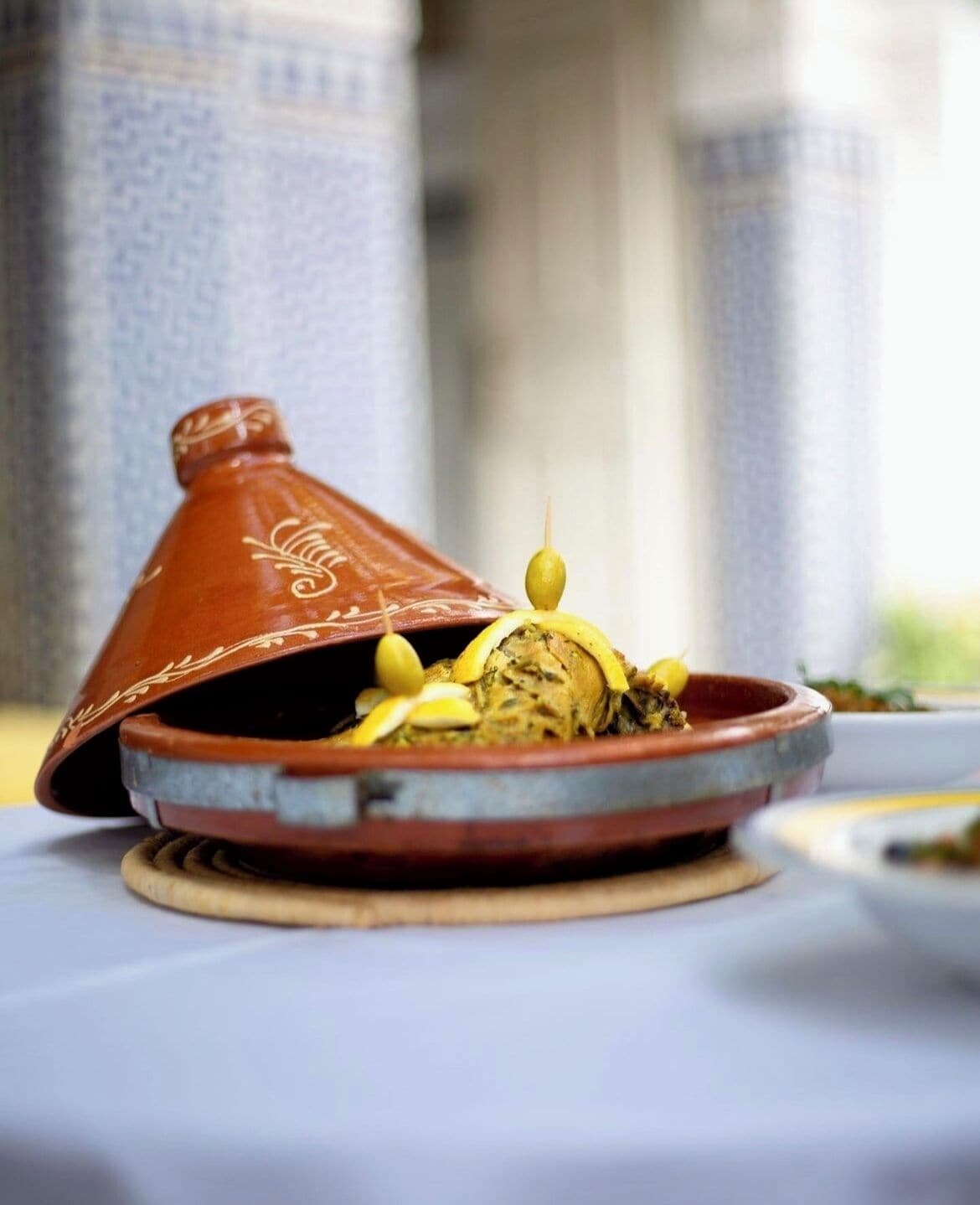 A traditional Moroccan tagine dish on a ceramic plate with a lid, placed on a table.