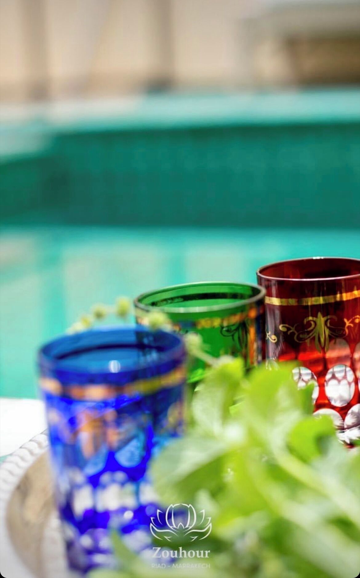 A poolside setting with colorful glassware and a logo for Zouhour.