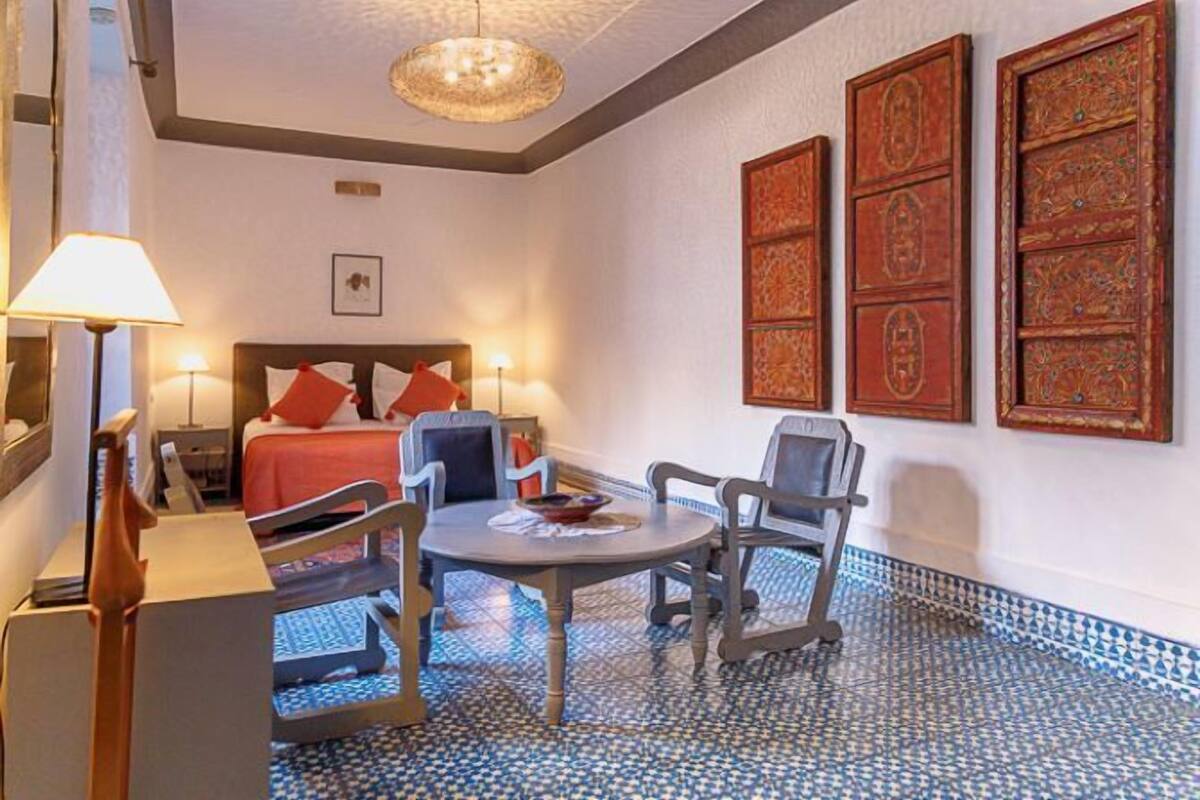 Una habitación de hotel con una cama, dos sillas, una mesita y una lámpara.