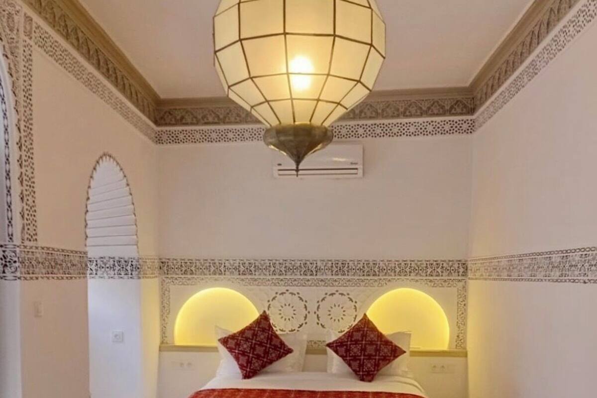 Una habitación con una cama, una lámpara colgante y diseños decorativos en las paredes.